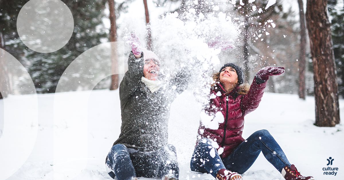 Two people dressed in winter gear play in the snow.